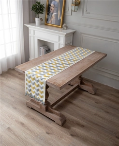 Detail of jacquard wave chenille table runner with blue pompom tassels on wooden surface