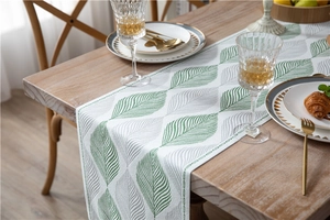 Detail of chenille jacquard table runner with green leaf patterns and tassel finish