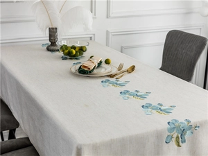 Close-up of blue floral embroidery on rustic linen rectangular tablecloth with fine texture