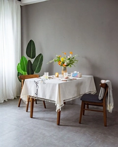Detail of bohemian cream tablecloth featuring fringe tassels and delicate floral embroidery