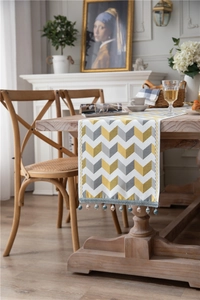 Detail of chenille table runner with wave patterns and fringe tassels on a wooden table