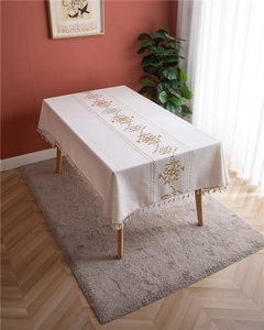 Detail of elegant beige rectangular tablecloth with gold embroidery and decorative tassels