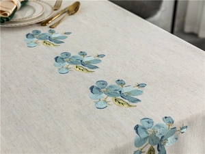 Close-up of blue floral embroidery and golden leaves on beige linen tablecloth