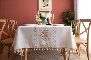 Close-up of vintage floral embroidery and beige tassel trim on a linen blend tablecloth