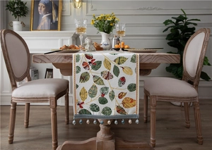 Detail of chenille table runner featuring leaf patterns, ladybugs, and beaded tassels