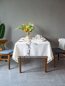 Close-up of beige tablecloth with embroidered cursive text and white tassel edge details