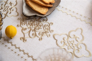 Detailed close-up of golden embroidery on cream linen tablecloth with vintage scroll patterns