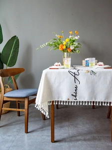 Macro detail of white linen tablecloth with floral embroidery and tassel fringe