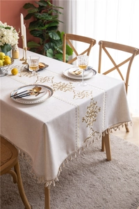 Detail of bohemian cream linen tablecloth with gold embroidery and fringe edges