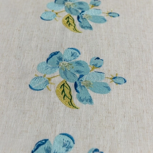 Close-up of blue floral embroidery on beige linen tablecloth with delicate stitching