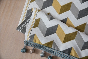 Close-up of jacquard chevron table runner with elegant pom-pom fringe on wood surface