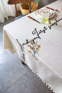 Detail of embroidered floral pattern and cursive text on beige tassel tablecloth