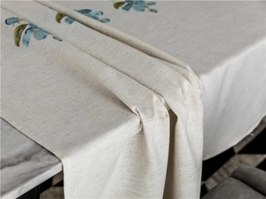 Detailed close-up of blue floral embroidery on a beige linen texture tablecloth