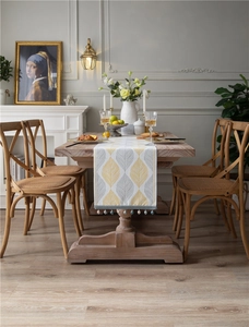 Detail of leaf pattern jacquard table runner with blue pom pom tassels on wooden table