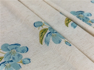 Detail of blue floral embroidery on beige cotton linen fabric with natural folding texture