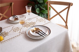 Close-up of beige linen tablecloth featuring golden floral patterns and elegant tassels