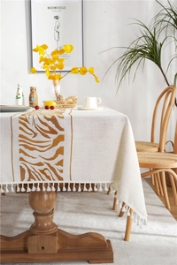 Detail of embroidered zebra pattern and white pom-pom tassels on linen tablecloth