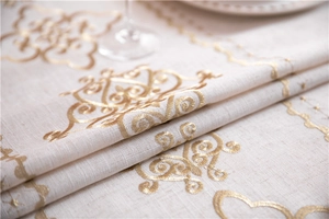 Close-up of beige linen tablecloth featuring intricate golden floral embroidery details