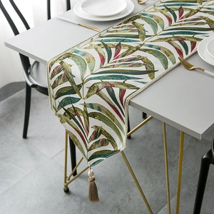Tropical leaf pattern chenille table runner with brown tassels on a grey dining table