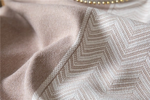 Close-up of cream beige wavy jacquard fabric texture with woven chevron fringe details