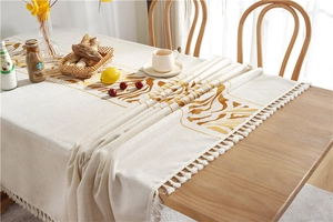 Detail shot of boho cream tablecloth with golden leaf patterns and fringe edges on wood