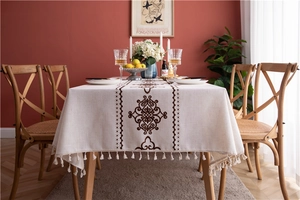 Close-up of cream rectangular tablecloth featuring brown floral embroidery and white tassels