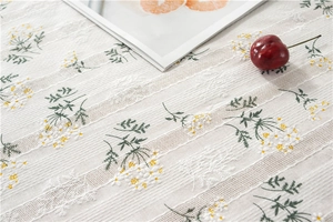 Close-up of lilac floral embroidery on white cotton lace tablecloth with striped texture