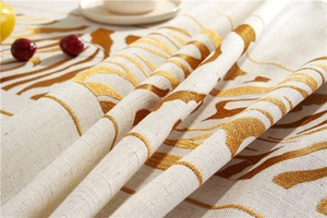 Detail of embroidered gold pattern and linen texture on cream rectangular tablecloth