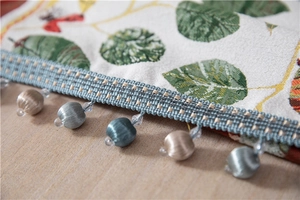 Detail of chenille table runner with fringe tassels and beads on wooden surface