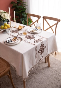 Close-up of beige linen tablecloth featuring brown embroidery patterns and fringe tassels