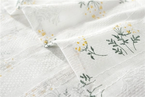 Detail of white cotton tablecloth showing green leaf and yellow floral embroidery