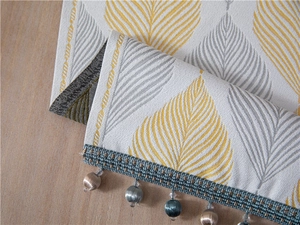 Macro view of modern chenille table runner with jacquard leaf patterns and soft tassels