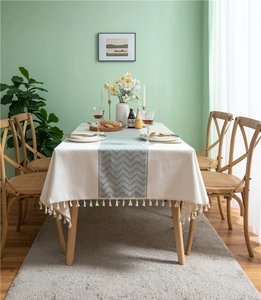 Macro detail of creamy white tablecloth with green wave pattern and tassel edges