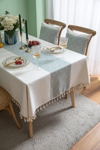 Detailed view of cream-colored tablecloth featuring green geometric patterns and elegant tassels