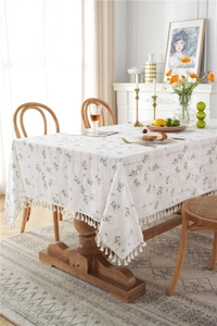 Detail of floral cotton tablecloth with delicate white fringe on a wooden table