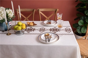 Detail of embroidered tablecloth with vintage brown scroll pattern and fringe edge