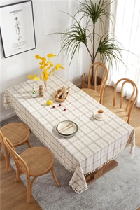Detail of beige plaid linen tablecloth with decorative white tassel trim and soft texture