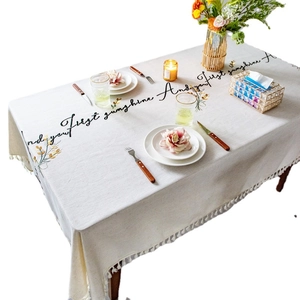 Rectangular beige linen tablecloth with embroidery flowers, text, and fringe tassels