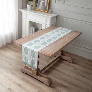Modern jacquard leaf chenille table runner with beaded fringe on a rustic wood table