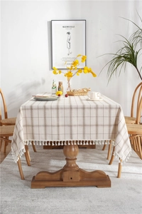 Close-up of beige plaid linen tablecloth featuring white cotton tassel edges on wood table