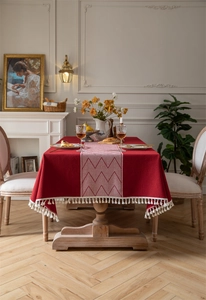 Detailed view of red jacquard tablecloth with geometric patterns and white fringe tassels