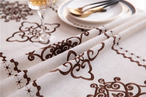 Detail of elegant beige cotton linen tablecloth with intricate dark brown embroidery