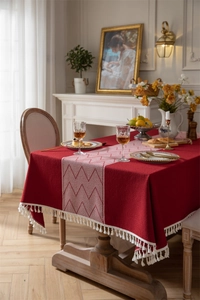Close-up of deep red jacquard tablecloth featuring white zigzag patterns and fringe edges