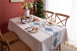 Detailed view of tablecloth with blue floral pattern and fringe edge on wooden table