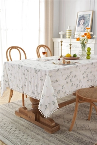 Detail of white cotton tablecloth with floral jacquard pattern and white pom-pom fringe
