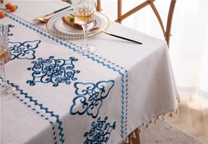 Detail of embroidered floral patterns and tassel edges on a beige linen tablecloth