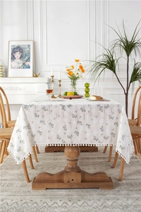 Macro detail of cotton floral tablecloth showing delicate yellow flowers and pom-pom trim