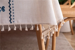 Detailed view of beige linen tablecloth with blue geometric embroidery and fringe