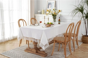 Detail view of white washed cotton tablecloth with delicate lace fringe on wooden dining table