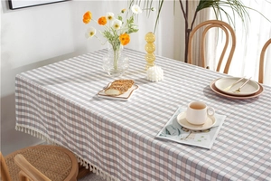 Detail of grey and pink plaid tablecloth with white cotton tassels on a wooden dining table
